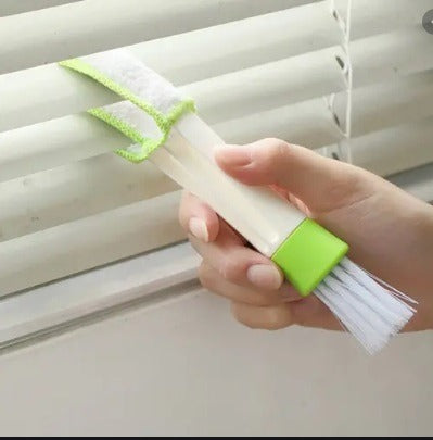 Hand using a cleaning brush with a green handle to clean blinds.