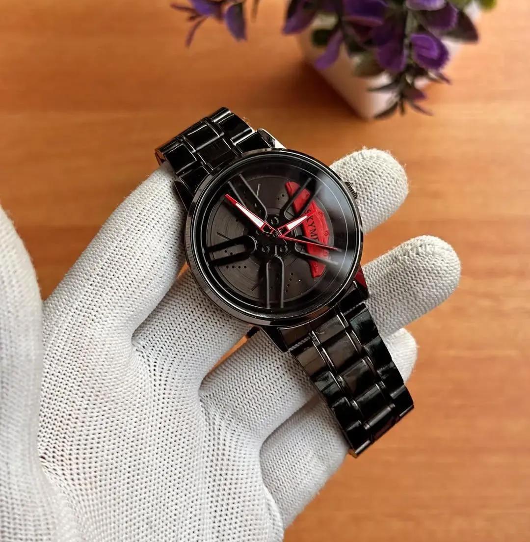 Black watch held by a gloved hand on a wooden surface with a blurred plant in the background
